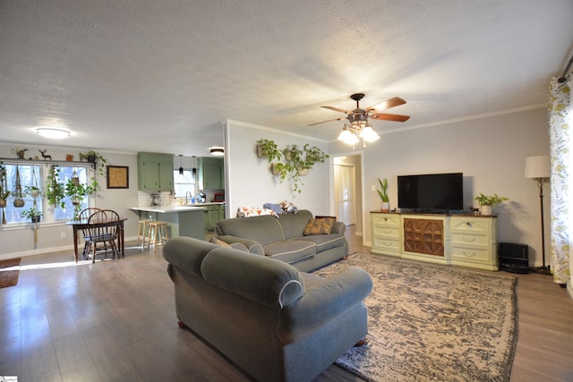 living area with a ceiling fan, a textured ceiling, ornamental molding, and wood finished floors