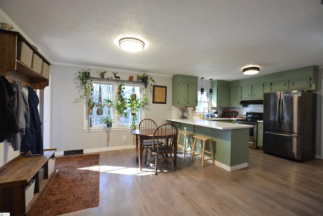 kitchen featuring a peninsula, stainless steel appliances, light countertops, a kitchen bar, and green cabinetry