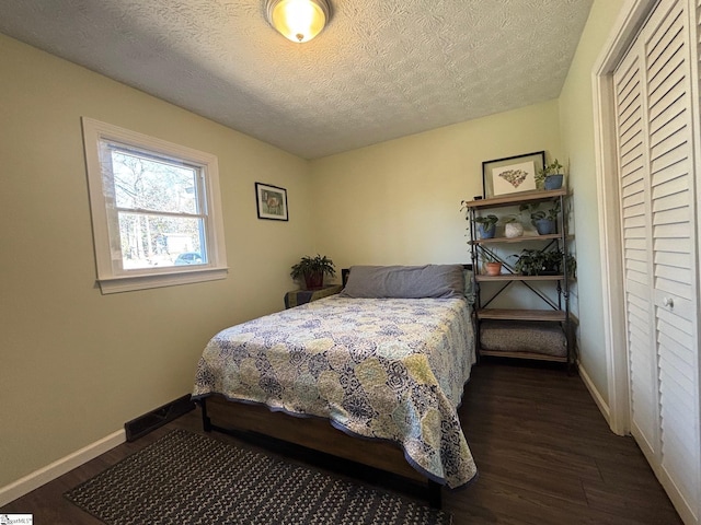 bedroom with a textured ceiling, dark wood finished floors, and baseboards