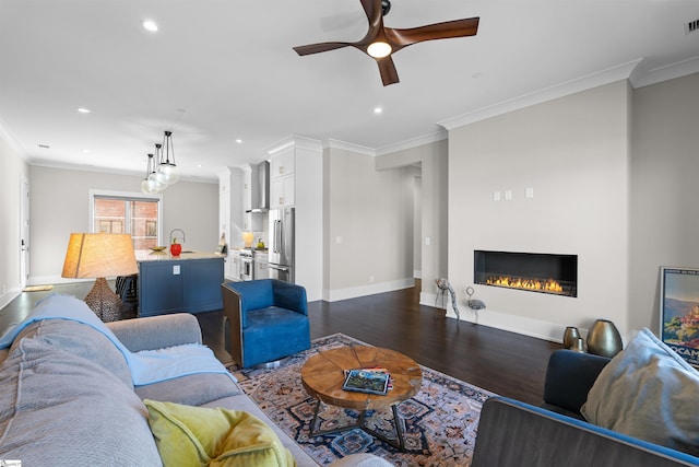 living room with ornamental molding, a glass covered fireplace, and dark wood finished floors