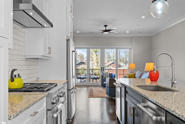 kitchen featuring appliances with stainless steel finishes, open floor plan, white cabinetry, wall chimney range hood, and light stone countertops