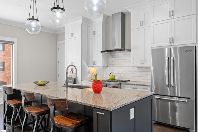 kitchen featuring high end fridge, wall chimney exhaust hood, a center island with sink, and white cabinets