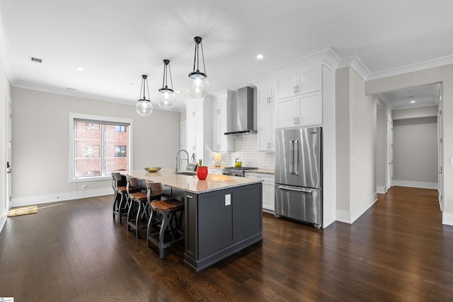 kitchen featuring high quality fridge, a kitchen island with sink, white cabinets, wall chimney range hood, and light stone countertops