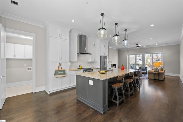 kitchen featuring open floor plan, wall chimney exhaust hood, a kitchen island with sink, and white cabinetry