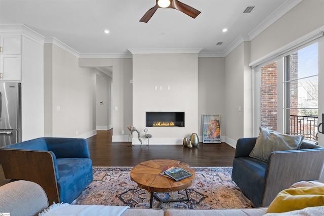 living room with visible vents, baseboards, a glass covered fireplace, dark wood-style floors, and ornamental molding