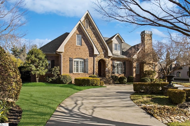 view of front of property featuring driveway, a front yard, a chimney, and brick siding