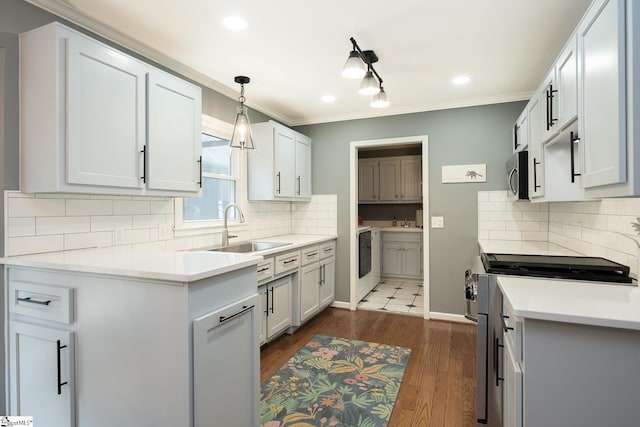 kitchen with washer / dryer, stainless steel appliances, light countertops, white cabinetry, and a sink