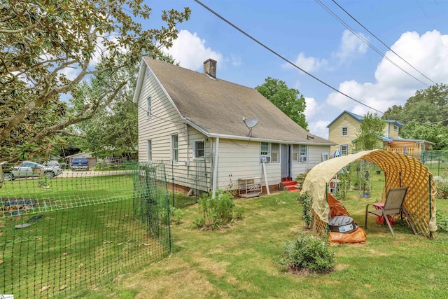 back of house with entry steps, roof with shingles, a chimney, and a yard