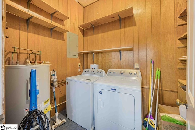 clothes washing area featuring washing machine and dryer, laundry area, wood walls, water heater, and electric panel