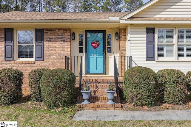 entrance to property featuring brick siding and roof with shingles