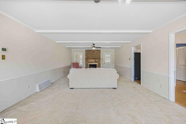 unfurnished living room with a wainscoted wall, beamed ceiling, a brick fireplace, and visible vents