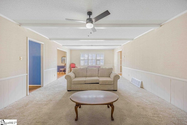 living area with wainscoting, beamed ceiling, and a textured ceiling