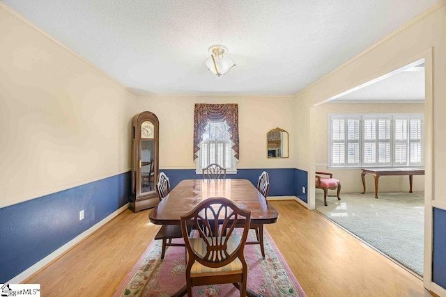 dining space with light wood finished floors, crown molding, baseboards, and a textured ceiling