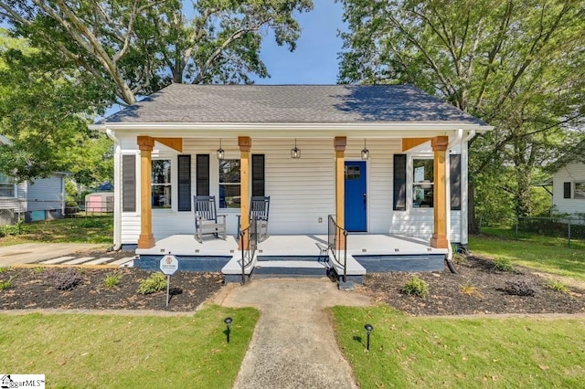 bungalow-style home with a shingled roof, fence, a porch, and a front yard