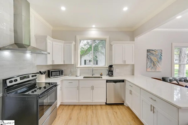 kitchen featuring stainless steel appliances, light countertops, a sink, wall chimney range hood, and a peninsula