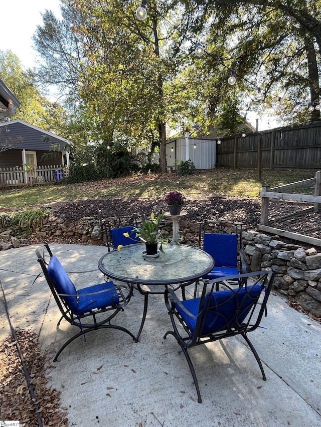 view of patio / terrace featuring a storage shed, outdoor dining area, an outdoor structure, and fence