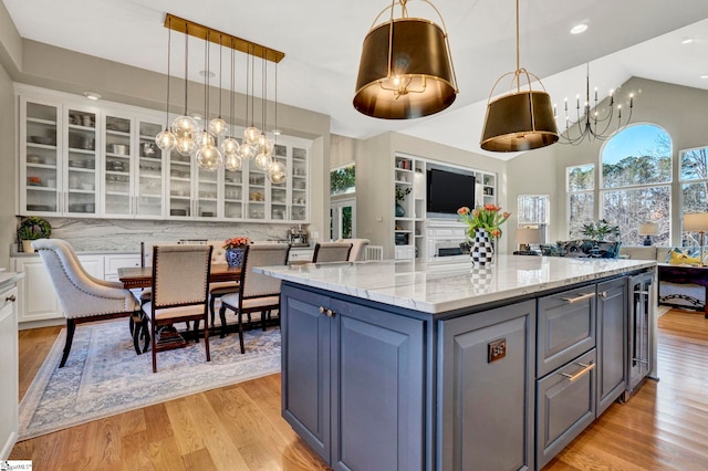 kitchen with light stone counters, a center island, light wood-style flooring, glass insert cabinets, and white cabinets