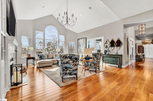 living area featuring baseboards, light wood-style flooring, high vaulted ceiling, and a notable chandelier