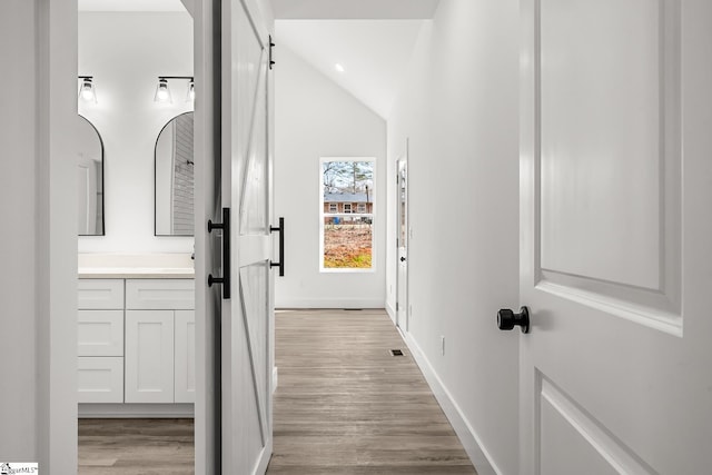 hall with light wood finished floors, a barn door, lofted ceiling, and baseboards