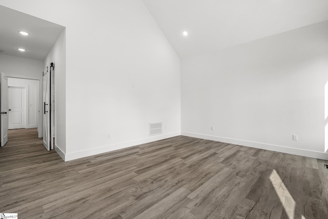 empty room with dark wood-style flooring, visible vents, baseboards, and a barn door