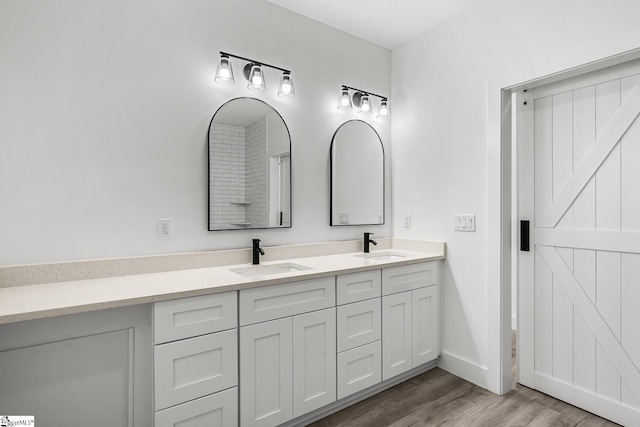 full bathroom with double vanity, a sink, baseboards, and wood finished floors