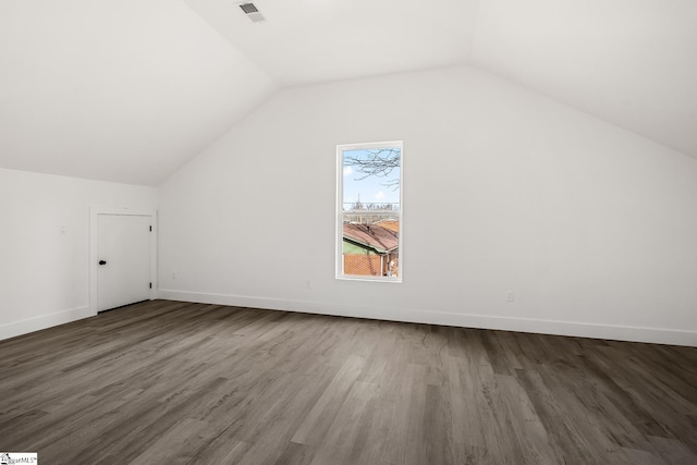 additional living space featuring vaulted ceiling, dark wood-type flooring, visible vents, and baseboards