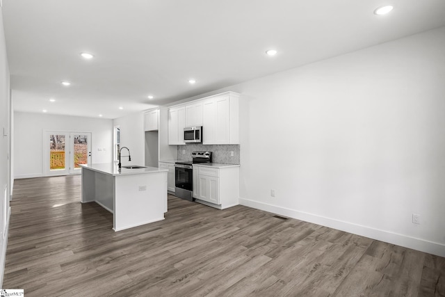 kitchen with stainless steel appliances, light countertops, a center island with sink, and white cabinets