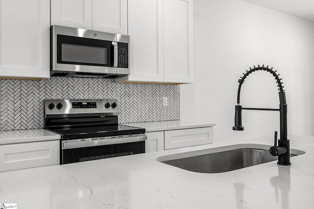 kitchen featuring stainless steel appliances, a sink, white cabinets, backsplash, and light stone countertops