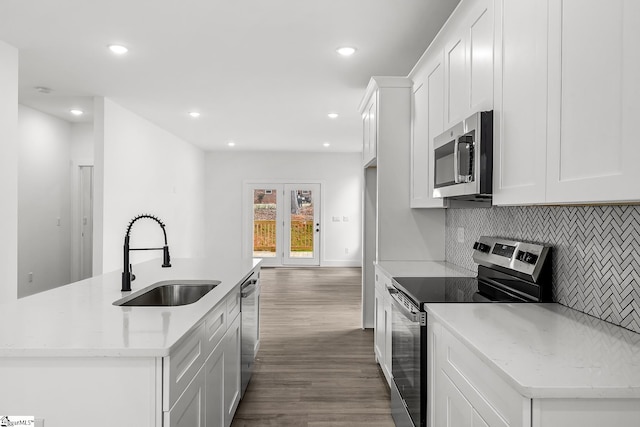 kitchen featuring an island with sink, light stone counters, stainless steel appliances, white cabinetry, and a sink