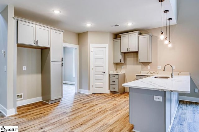 kitchen featuring decorative light fixtures, a sink, light stone countertops, light wood-type flooring, and a peninsula