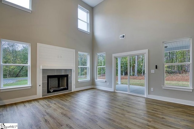 unfurnished living room featuring visible vents, a high ceiling, a tiled fireplace, wood finished floors, and baseboards