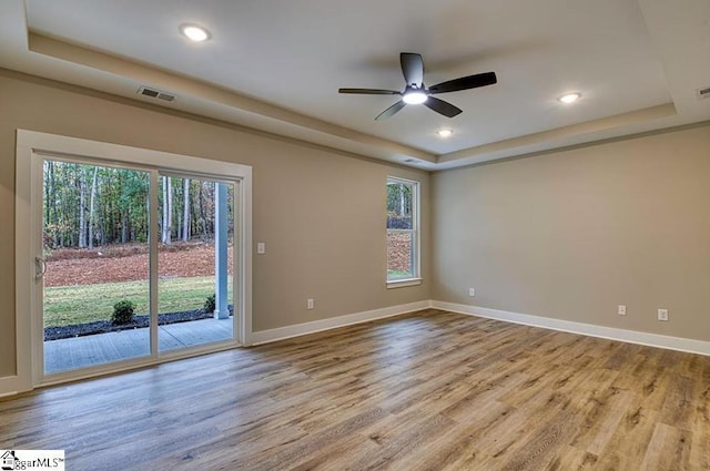 unfurnished room with light wood-style floors, a raised ceiling, and visible vents