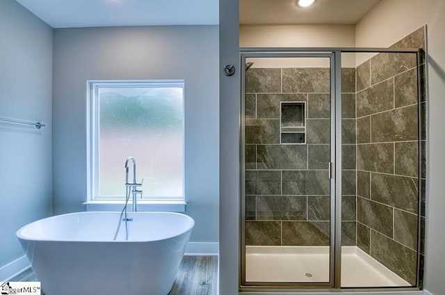 bathroom featuring a stall shower, a soaking tub, baseboards, and wood finished floors