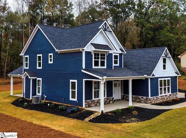 view of front of property with board and batten siding, stone siding, central AC, and a front lawn