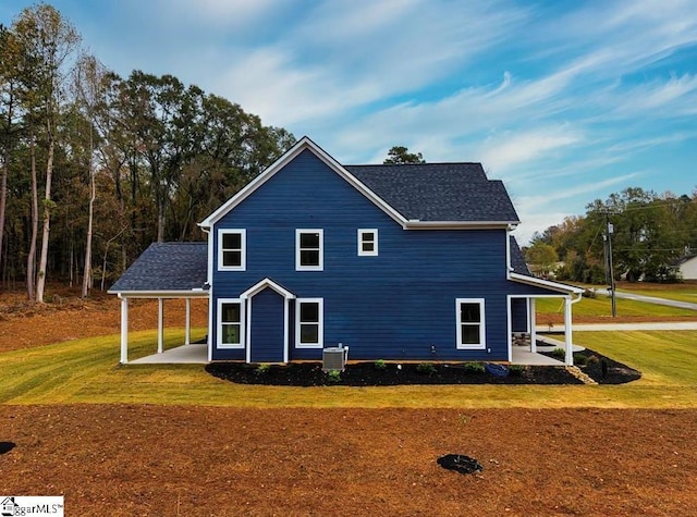 exterior space with central air condition unit, a shingled roof, a lawn, and a patio