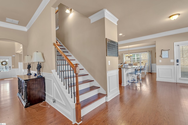 staircase with arched walkways, a wainscoted wall, crown molding, visible vents, and wood finished floors