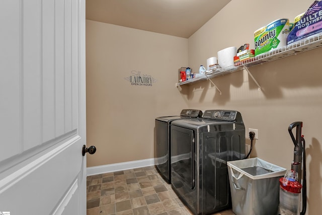 washroom featuring laundry area, baseboards, stone finish flooring, and washing machine and clothes dryer