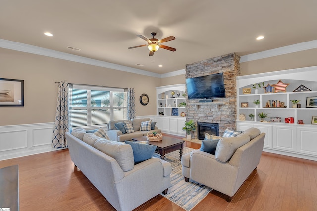 living room featuring built in features, visible vents, light wood-style floors, and a stone fireplace