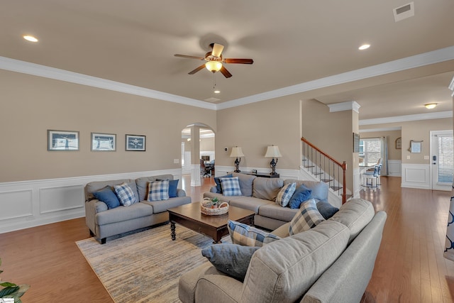 living area with arched walkways, ceiling fan, visible vents, stairs, and light wood-type flooring