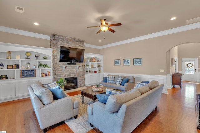 living room featuring built in shelves, arched walkways, a fireplace, light wood finished floors, and visible vents