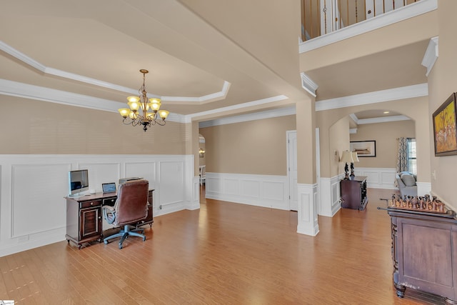 office with arched walkways, a chandelier, light wood-style flooring, a decorative wall, and a tray ceiling