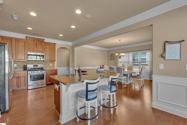 kitchen featuring an island with sink, light stone countertops, stainless steel appliances, pendant lighting, and a sink