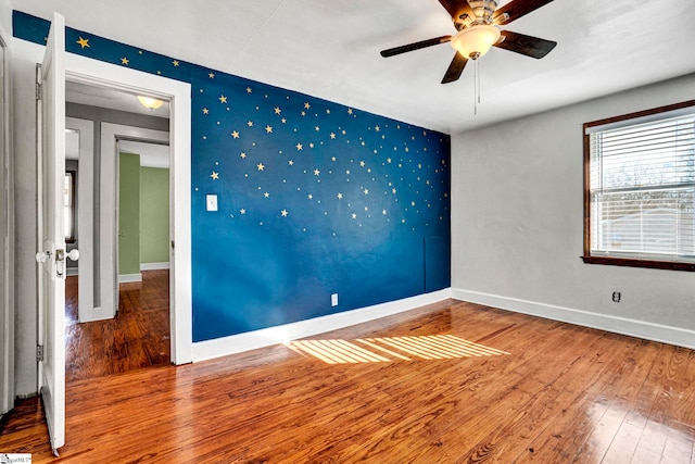 empty room with baseboards, an accent wall, wood finished floors, and wallpapered walls