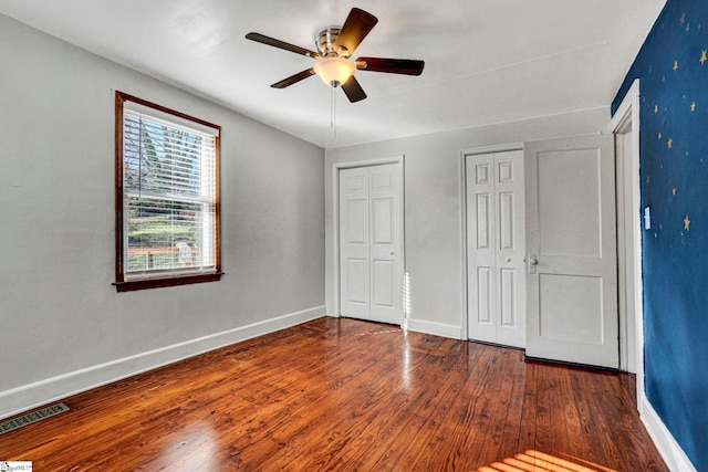 unfurnished bedroom featuring baseboards, visible vents, multiple closets, and wood finished floors