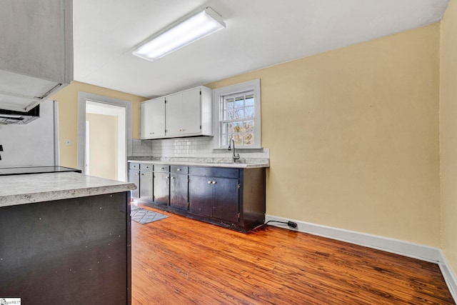 kitchen featuring light countertops, decorative backsplash, light wood-style floors, a sink, and baseboards