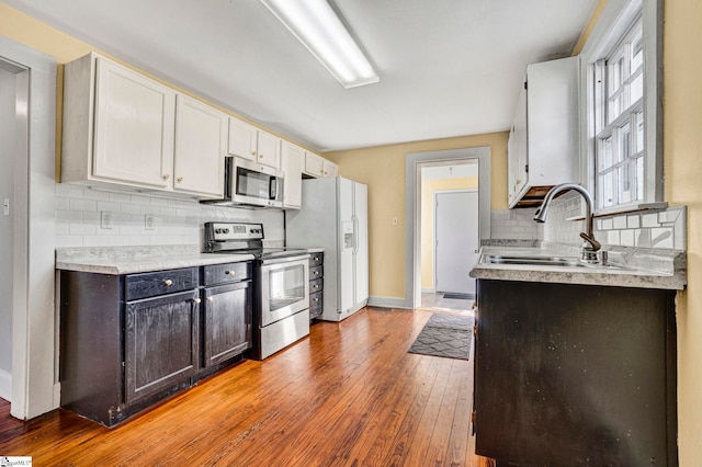 kitchen with decorative backsplash, appliances with stainless steel finishes, light countertops, light wood-type flooring, and a sink