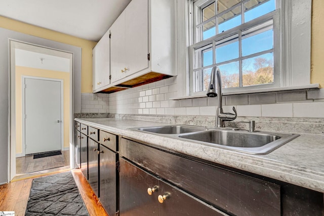 kitchen featuring a sink, white cabinetry, light countertops, light wood-type flooring, and tasteful backsplash