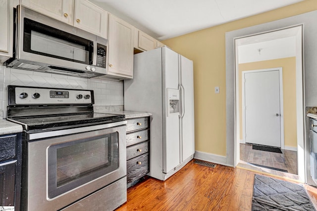 kitchen with light wood finished floors, stainless steel appliances, light countertops, white cabinetry, and backsplash