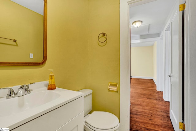 half bath featuring baseboards, vanity, toilet, and wood finished floors