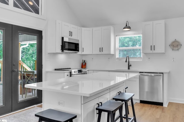 kitchen with stainless steel appliances, a sink, white cabinetry, a center island, and a kitchen bar